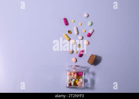 White and yellow pills scattered near opened bottle on blue background. Concept of medical treatment with medicine, vitamins or supplements in capsule Stock Photo