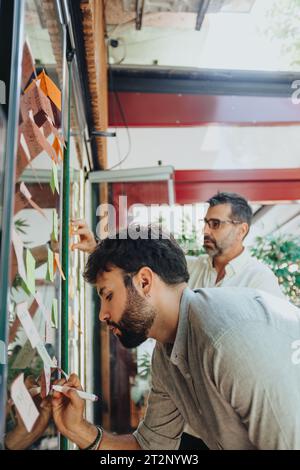Team of professionals brainstorm ideas and discuss strategies behind a glass wall, utilizing post-it notes for problem-solving in a modern office. Stock Photo