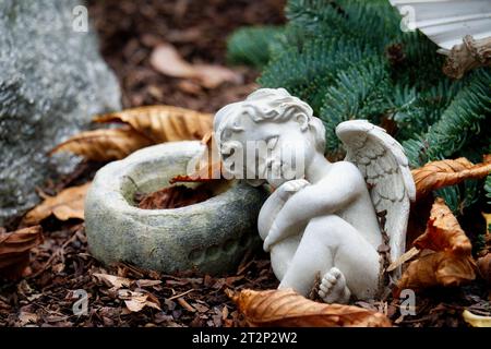 cute little white putto sleeping on a grave with autumn leaves in a cemetery Stock Photo