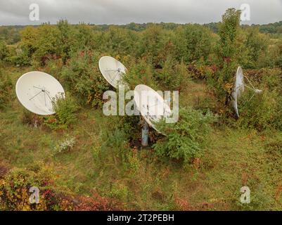 Abandoned satellite dish broadcast antenna in a field with overgrown vegetation. Stock Photo