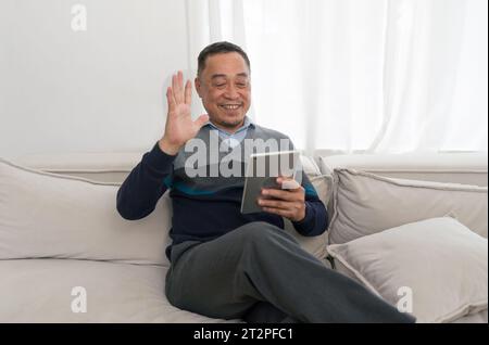A casually dressed man sits comfortably on a plush grey couch, his attitude relaxed yet focused. His eyes are warm, inviting and fully engaged with th Stock Photo