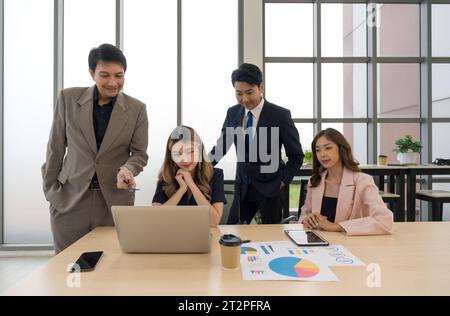 Business professionals collaborating with enthusiasm while examining data on a laptop in a contemporary office setting. Stock Photo