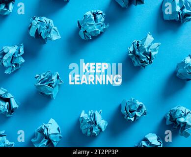 Keep learning message with crumpled blue paper balls on blue background. Continuous education and learning concept. Stock Photo