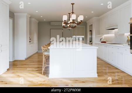 Traditional white kitchen with long island and wooden chairs with varnished wood flooring.  Stock Photo