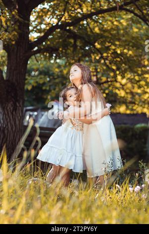 Two little girls, sisters in white dresses hugging Stock Photo