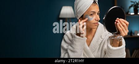 Hygiene, beautician, makeup and face care concept. Patches for eyes. Hispanic woman with towel on her head glues transparent patches to skin under her Stock Photo