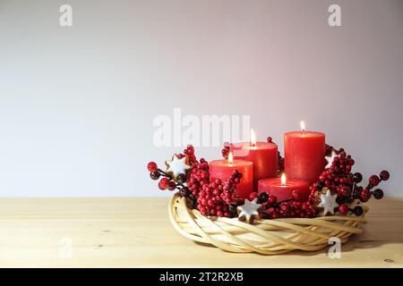 Fourth advent with four lit red candles in a natural willow wicker wreath with cinnamon star cookies and artificial berries, holiday decoration, copy Stock Photo