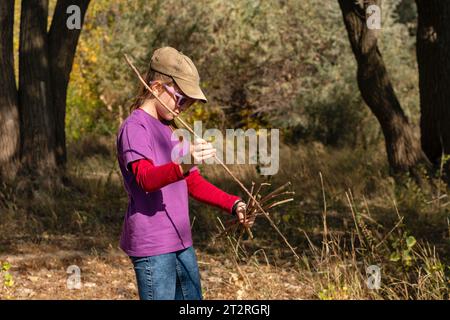 Teenage girl, dressed in comfortable suit, curiously collects firewood for fire while hiking in nature. Stock Photo