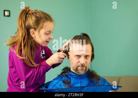 Joyful girl playfully cuts her father's hair at home, creating a bond and memories through a fun and innocent hair transformation session. Stock Photo