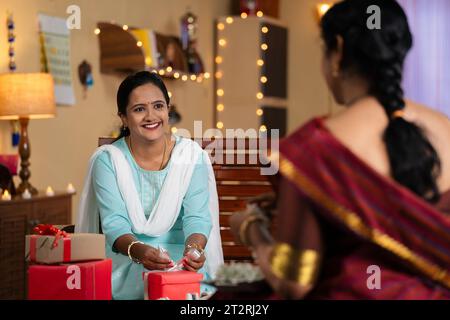 Shoulder shot mother and happy daughter packing gift for diwali festival celebration at home - concept of festive preparation, family support and Stock Photo