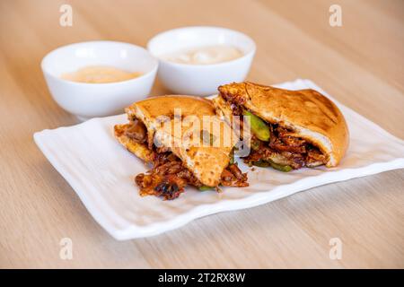 Italian pieces of shawarma full of peppers and BBQ sauces with chicken on wooden table with dips Stock Photo