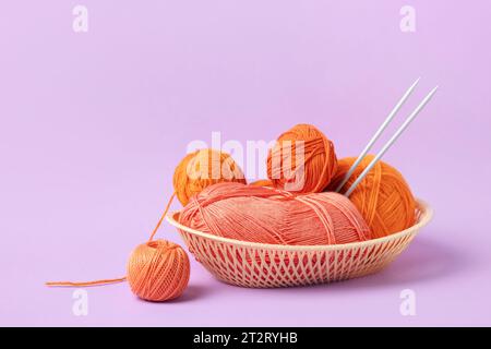 Orange and pink knitting balls in a basket with knitting needles on lilac background. Set for the hobby of knitting warm clothes or toys. Concept need Stock Photo