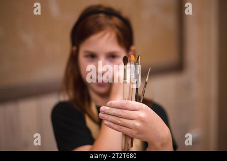 A girl in a creative workshop holds brushes for coloring a clay product Stock Photo