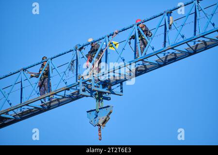 construction workers, with harness tied in, walking along the vertical structure of a crane Stock Photo