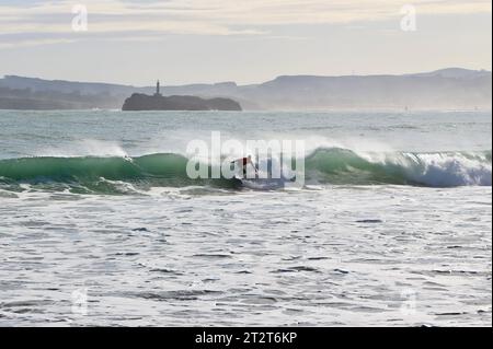 A surfer with Mouro Island at the entrance to the bay with strong waves on a sunny autumn morning Sardinero Santander Cantabria Spain Stock Photo