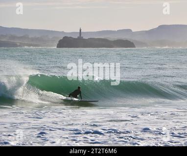 A surfer with Mouro Island at the entrance to the bay with strong waves on a sunny autumn morning Sardinero Santander Cantabria Spain Stock Photo