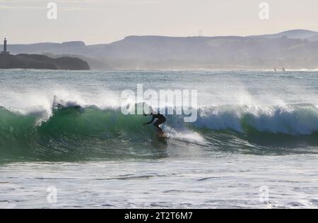 A surfer with Mouro Island at the entrance to the bay with strong waves on a sunny autumn morning Sardinero Santander Cantabria Spain Stock Photo