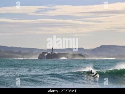 A surfer with Mouro Island at the entrance to the bay with strong waves on a sunny autumn morning Sardinero Santander Cantabria Spain Stock Photo