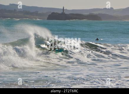 A surfer with Mouro Island at the entrance to the bay with strong waves on a sunny autumn morning Sardinero Santander Cantabria Spain Stock Photo