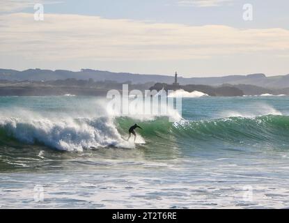 A surfer with Mouro Island at the entrance to the bay with strong waves on a sunny autumn morning Sardinero Santander Cantabria Spain Stock Photo