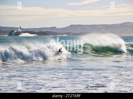 A surfer with Mouro Island at the entrance to the bay with strong waves on a sunny autumn morning Sardinero Santander Cantabria Spain Stock Photo