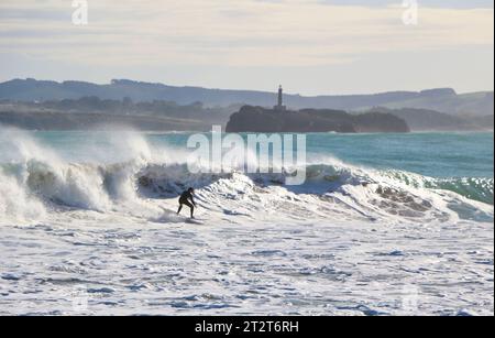 A surfer with Mouro Island at the entrance to the bay with strong waves on a sunny autumn morning Sardinero Santander Cantabria Spain Stock Photo