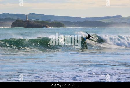 A surfer with Mouro Island at the entrance to the bay with strong waves on a sunny autumn morning Sardinero Santander Cantabria Spain Stock Photo