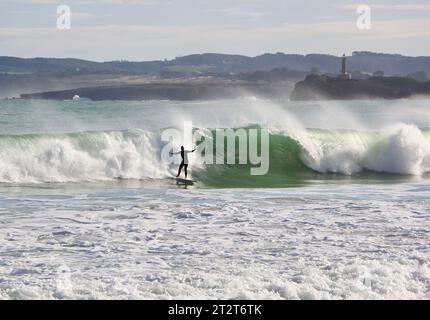 A surfer with Mouro Island at the entrance to the bay with strong waves on a sunny autumn morning Sardinero Santander Cantabria Spain Stock Photo