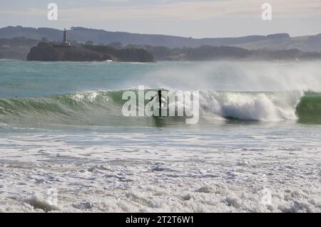 A surfer with Mouro Island at the entrance to the bay with strong waves on a sunny autumn morning Sardinero Santander Cantabria Spain Stock Photo