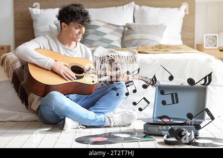 Young man listening to music and playing guitar in bedroom Stock Photo