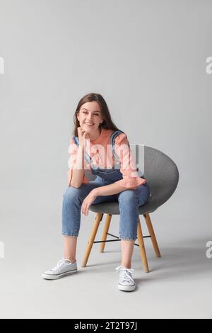 Beautiful happy young woman sitting on modern chair against grey background Stock Photo