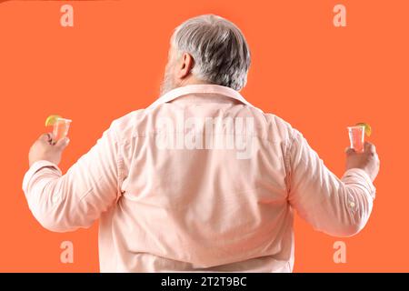 Portrait of senior man with shots of tequila on orange background, back view Stock Photo