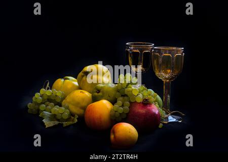 a still life with quinces, grapes, pears and apples with two glasses of wine and black background Stock Photo