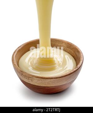 condensed milk pouring into wooden bowl isolated on white background Stock Photo
