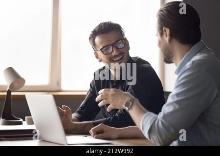 Two millennial businessmen having discussion seated at desk with laptop Stock Photo