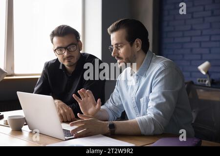 Male colleagues discussing new project in office with laptop Stock Photo
