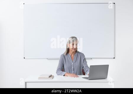 Professor sitting near laptop at desk in classroom Stock Photo