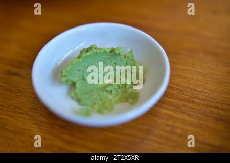 Green wasabi sauce or paste in bowl, with chopsticks or spoon over plain colourful background. selective focus Stock Photo