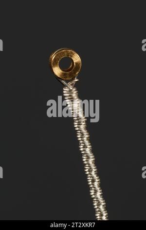 Bottom mount of a silver guitar string on a dark background. Macro photography Stock Photo
