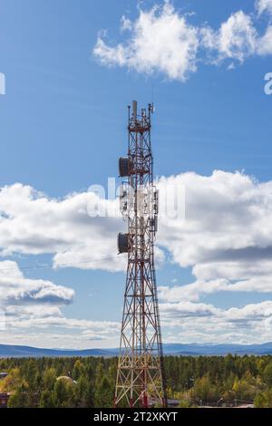 Telecommunication tower with various antennas against the background of a blue cloudy sky and mountains in the distance Stock Photo