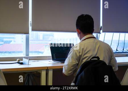 An IT software developer is seen working behind a laptop while looking out an office window Stock Photo