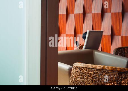 A solitary man sitting on a chair, engrossed in using his mobile phone, with a well-composed copy space for text Stock Photo