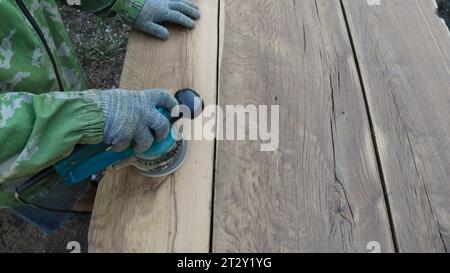 solid wood in the process of sanding a textured surface using an emery machine in the hands of a woodworker, a carpenter processes oak boards Stock Photo