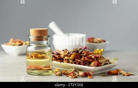 Essential oil or herbal tincture into a glass bottle. The mix of dried healthy medicinal herbs and healing plants on a grey stone table. Copy space. Stock Photo