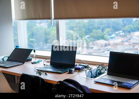 Row of laptops resting on office desk in front of window after work hours Stock Photo