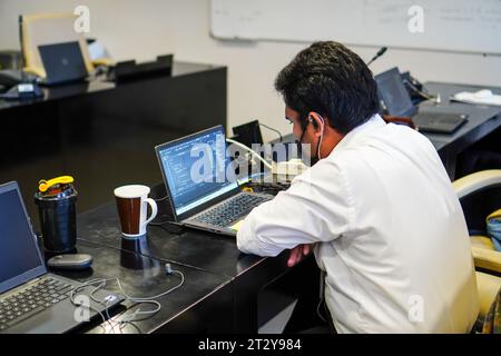 Office scene: IT specialist with glasses working on a laptop seen from behind Stock Photo