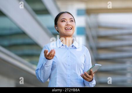 Japanese employee lady talking on smartphone with wireless earphones outside Stock Photo