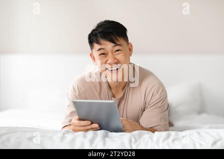 Happy asian man using digital tablet in bed Stock Photo