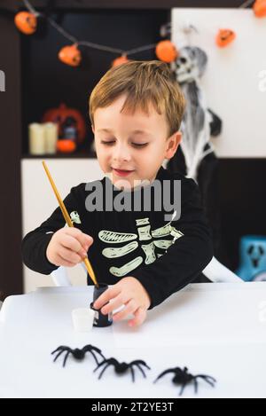 A child dressed as a skeleton shows spider and ghost crafts. Halloween party Stock Photo