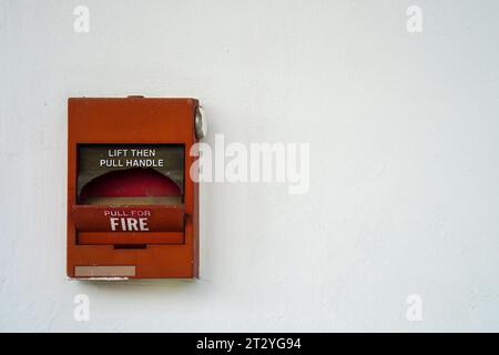 Damaged red fire alarm box with clean white wall as background with copy space for text Stock Photo